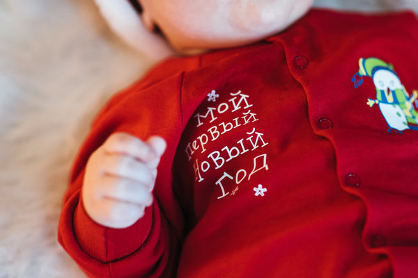 Red baby outfit with embroidered text and cartoon character on a soft surface