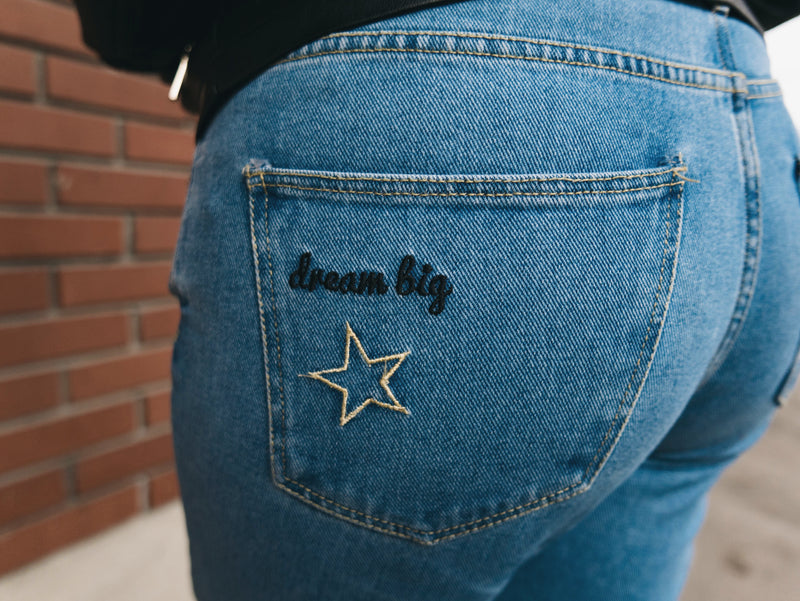 Blue jeans with 'dream big' and star embroidery on a brick wall background
