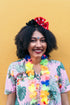 Woman wearing a colorful shirt and lei against a yellow wall