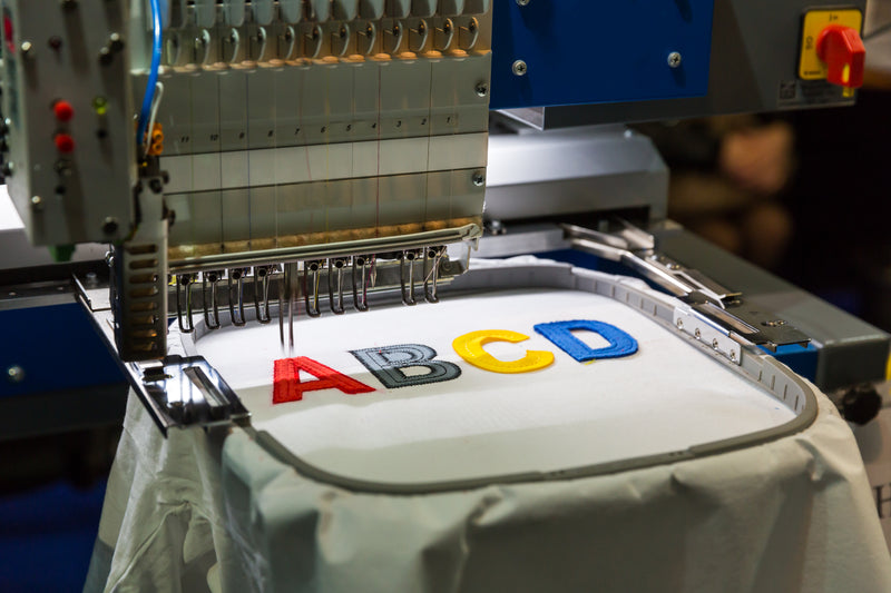 Embroidery machine with colorful letters 'ABCD' on a piece of fabric.