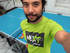 Man in a green shirt with a brand logo taking a selfie in front of a blue ping pong table.